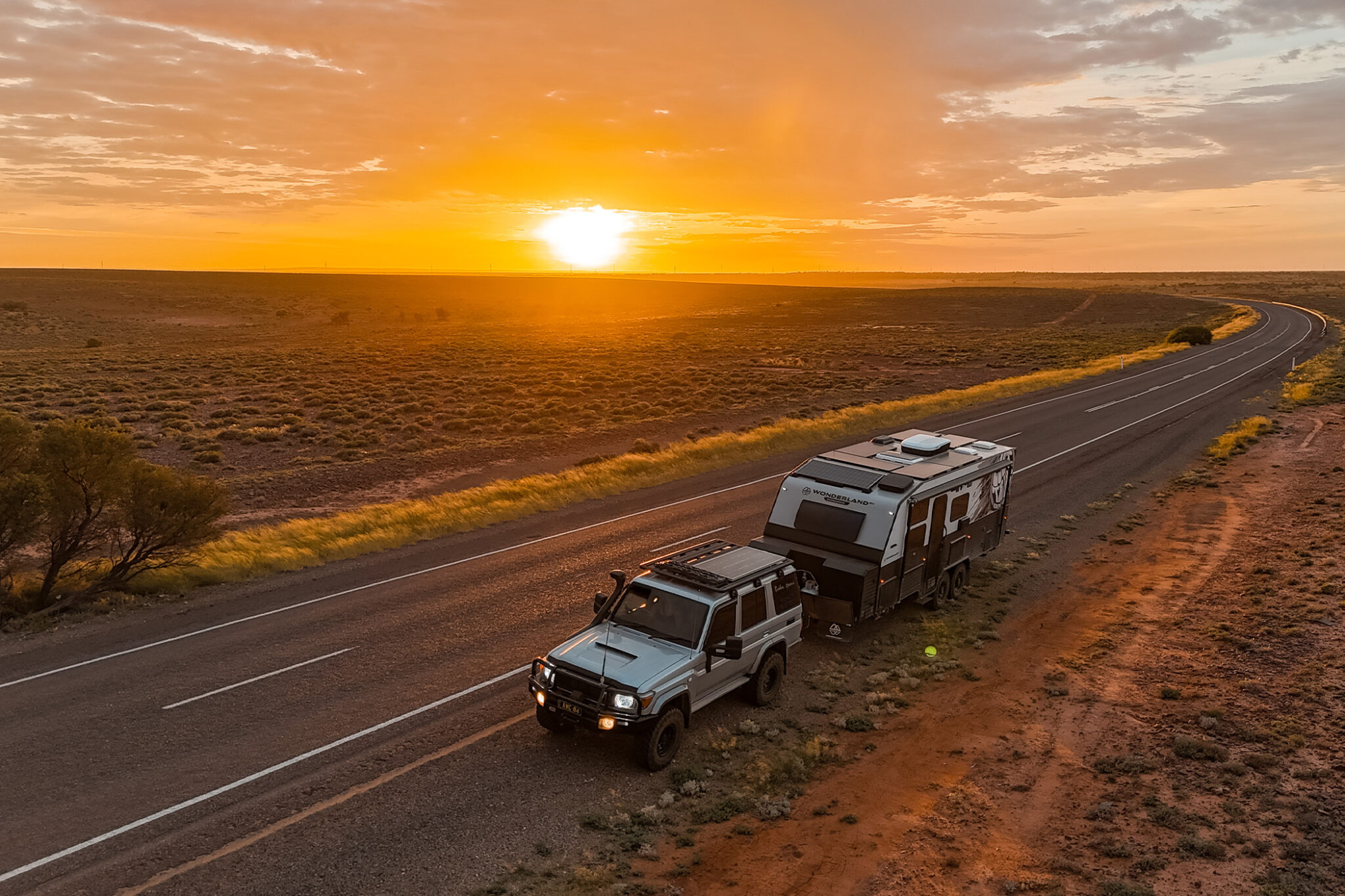 A beautiful sunset in the Australian outback with a Wonderland caravan being towed along a long road