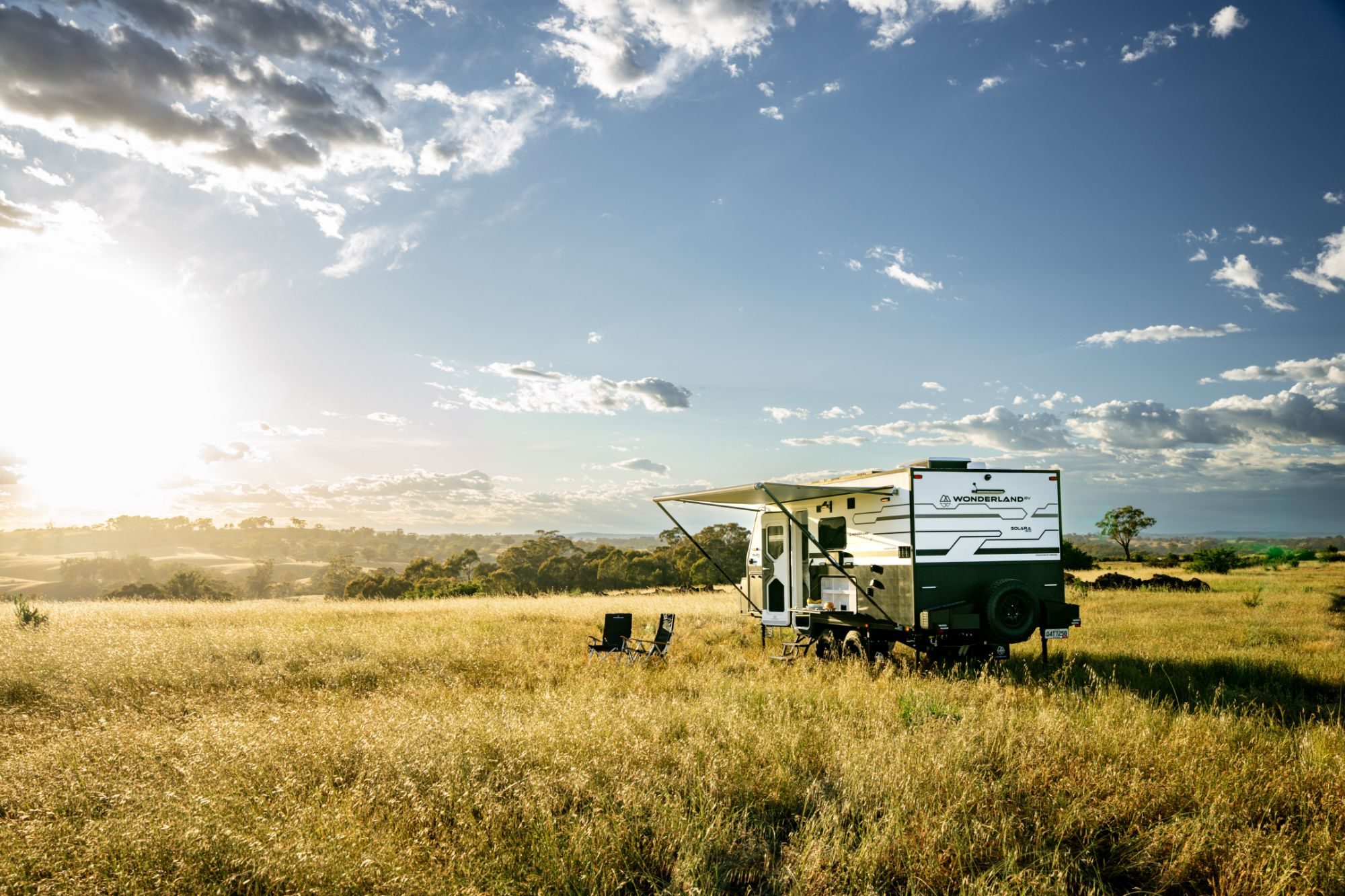 Wonderland RV Solara caravan set up with the awning out and two camp chairs in a golden paddock