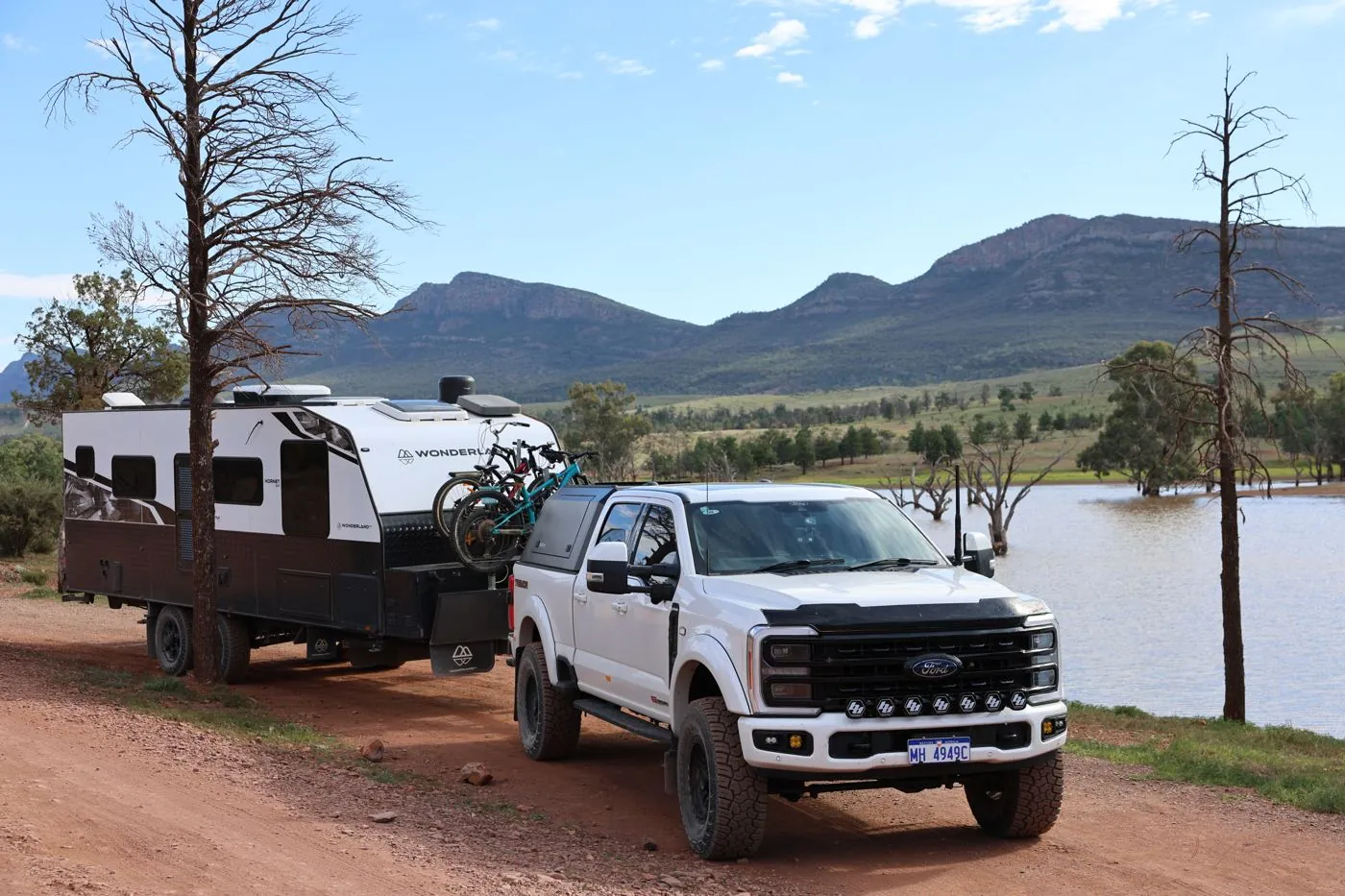 White ute towing a Wonderland RV caravan beside a lake with mountains behind