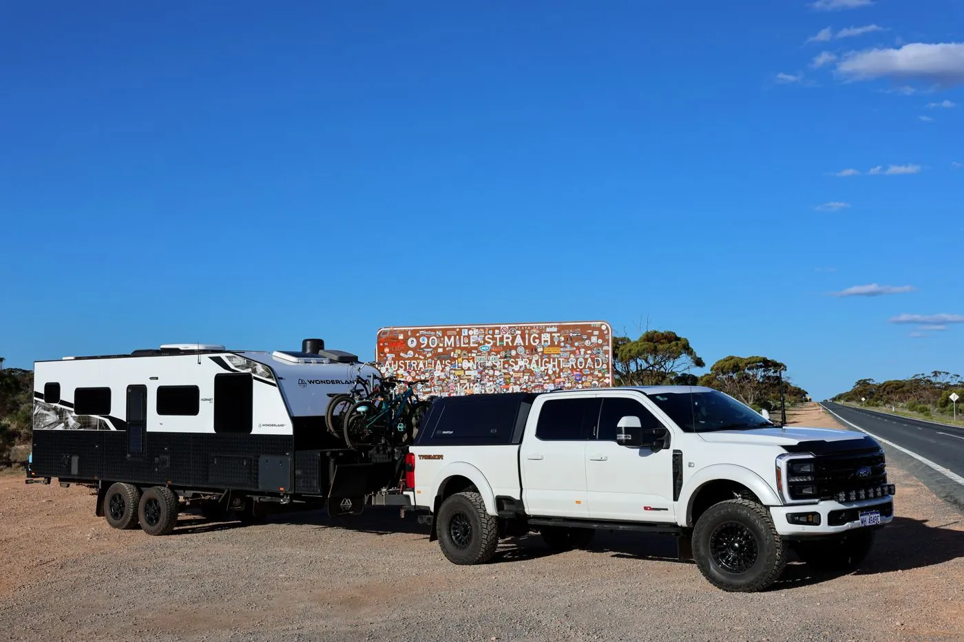 White ute and Wonderland RV caravan stopped beside a sign on an outback highway