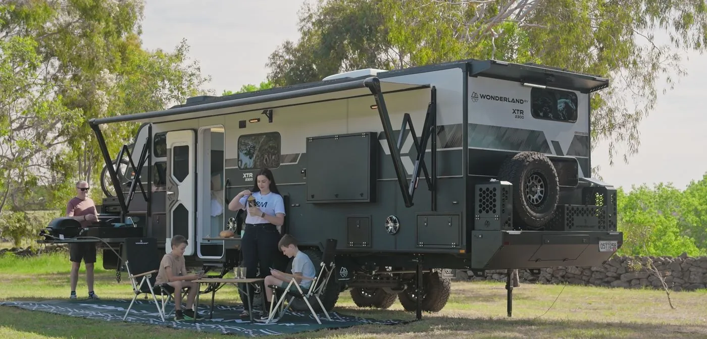 Family relaxing under the awning of a Wonderland RV caravan at a grassy campsite