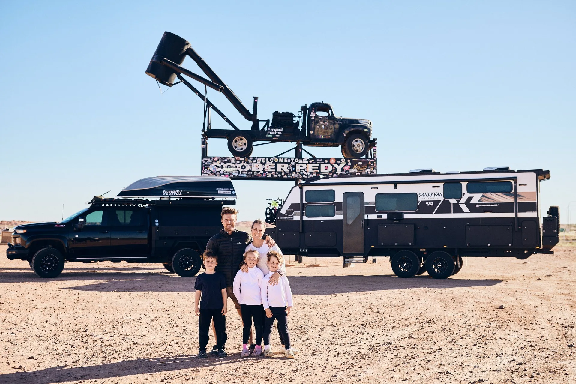 Jess, Doug and their three children with their caravan at the Coober Pedy sign